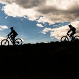 Two silhouettes of people riding bike