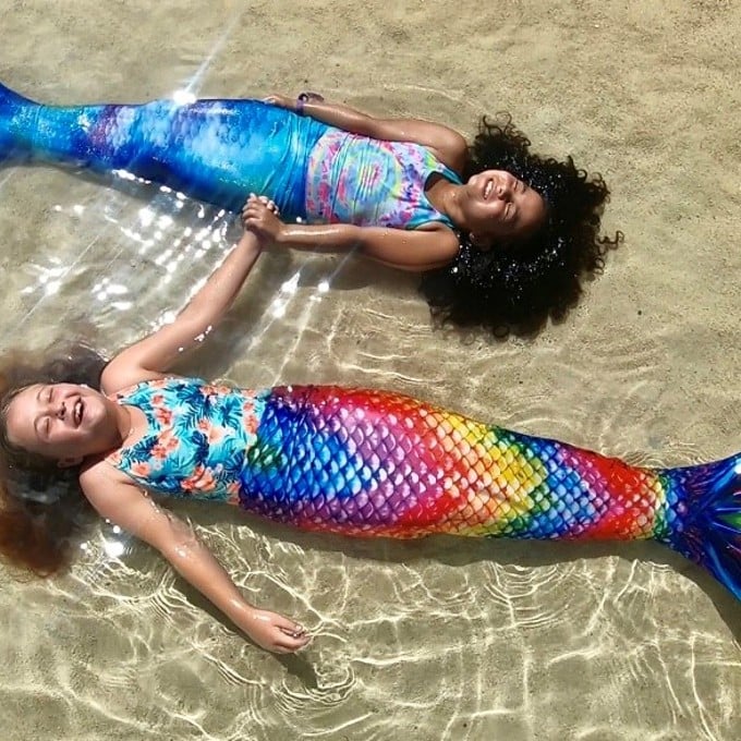 Two mermaids laying in water
