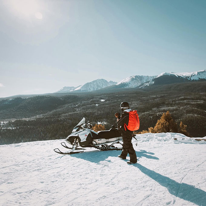 Person Walking Towards Snowmobile in Mountains